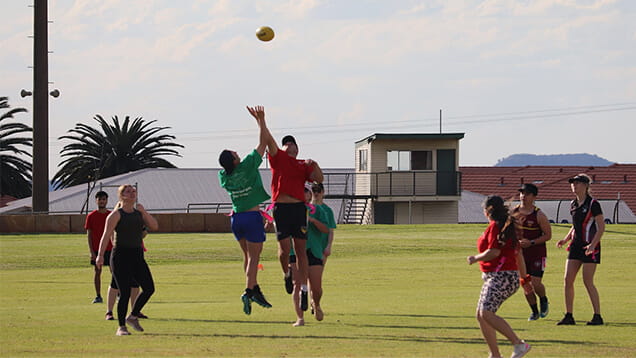 A group of people playing a game on a grassy field, with two players jumping to catch a ball.