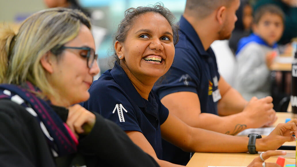 People sitting at a table, engaged in discussion, with one person smiling broadly.