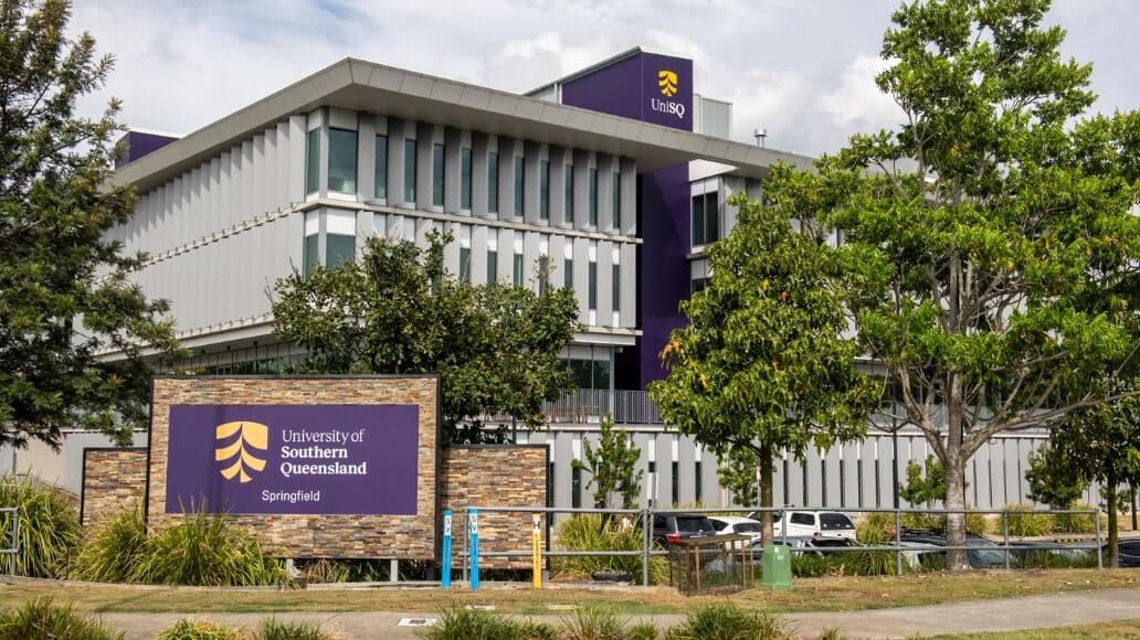 University of Southern Queensland Springfield campus building with trees and a prominent sign in the foreground.