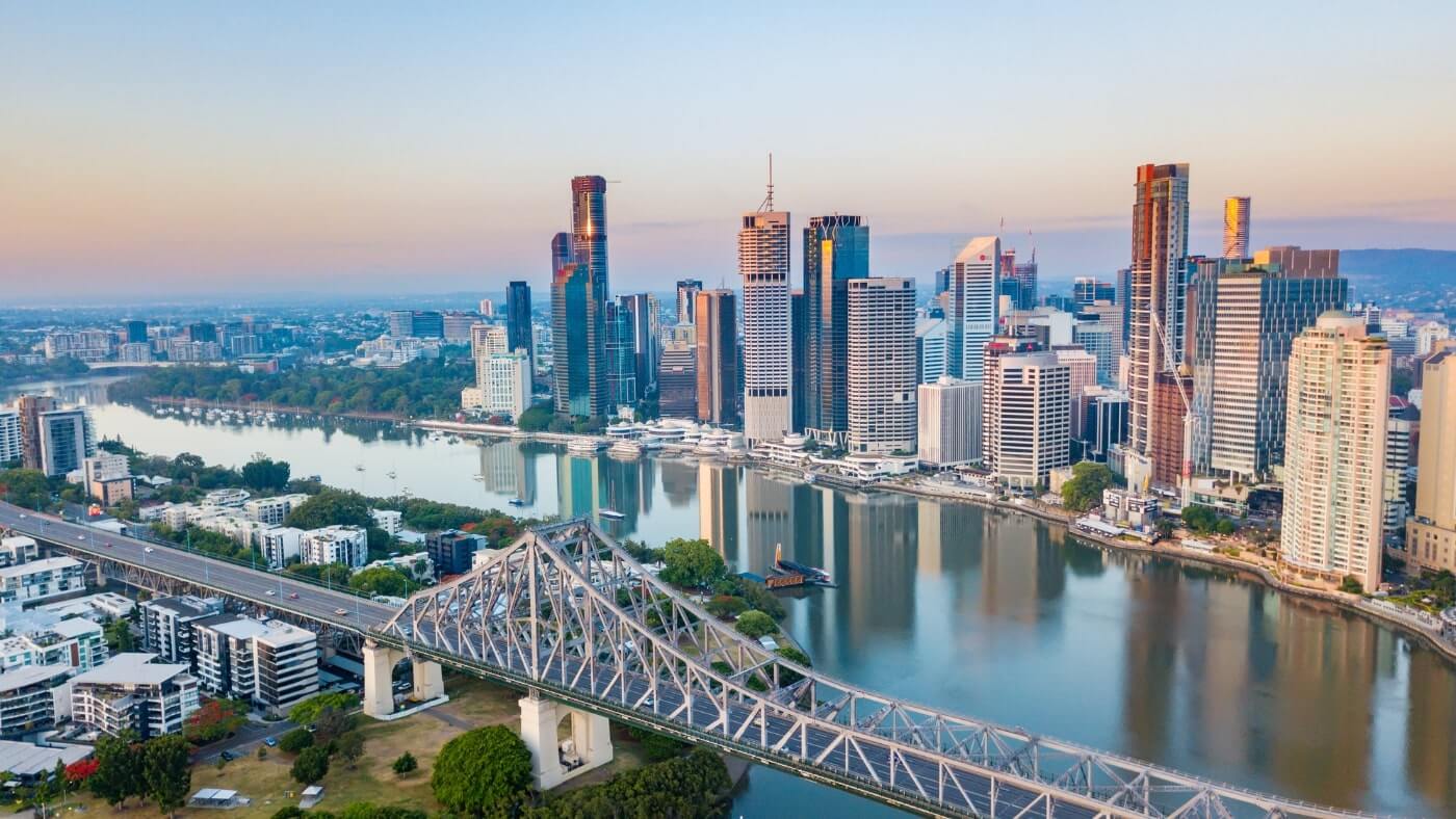 Aerial view of Brisbane city skyline with modern high-rise buildings, the Brisbane River, and Story Bridge in the foreground during daytime.