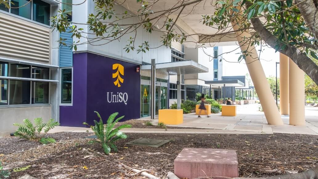 Exterior view of the UniSQ building with visible signage, large windows, and surrounding landscaping.