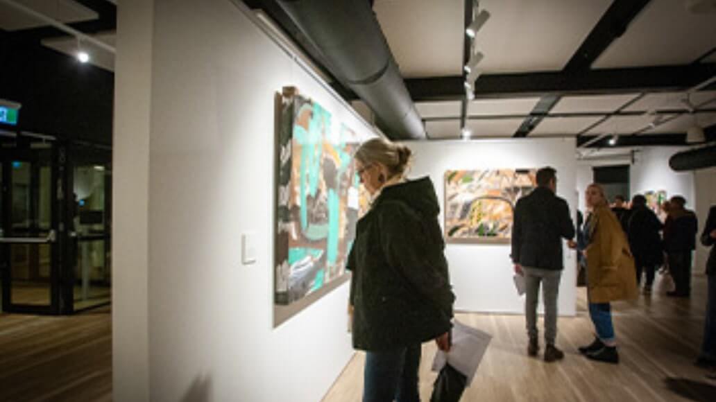 People viewing art in a modern gallery with bright lighting and wooden floors.