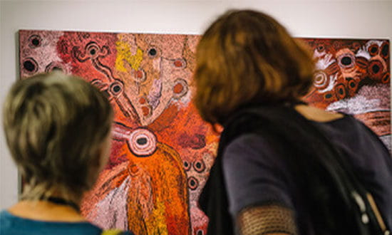 Two people stand in front of an abstract painting with vibrant red and orange patterns.