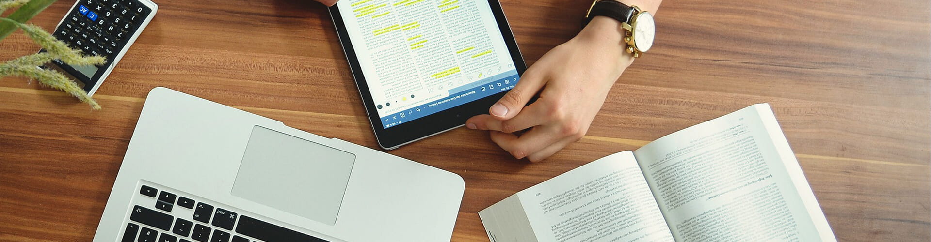 Two individuals engaged in a handshake over a desk with a laptop, tablet, calculator, and documents.