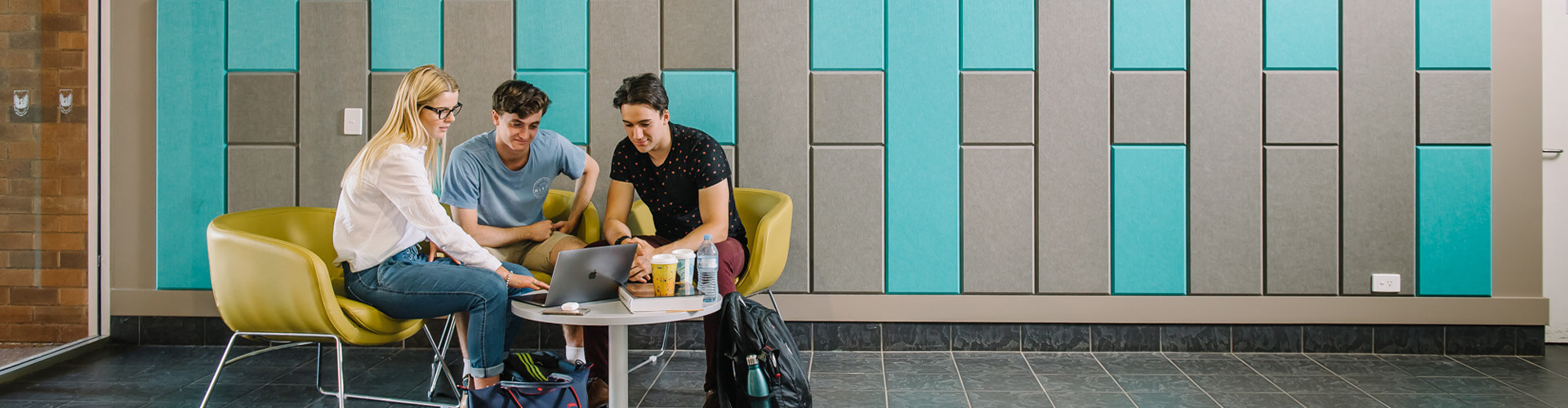 Three individuals engaged in a discussion at a small round table in a modern lobby with turquoise wall accents.