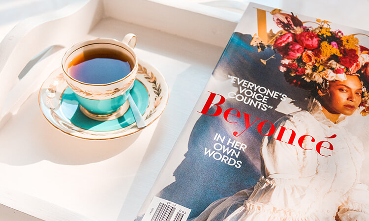 A cup of tea on a tray beside a magazine featuring beyoncé.