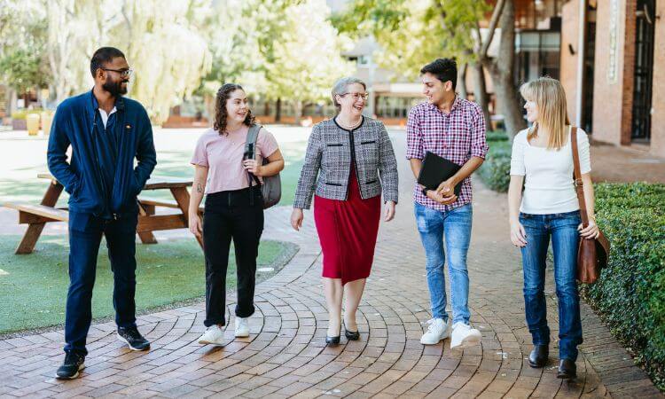 The UniSQ Vice-Chancellor and four university students walking on a footpath, smiling with each other.