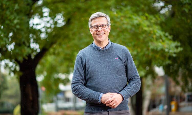 Professor Robbie Girling stands smiling at the camera. He is wearing glasses and anavy blue sweater.