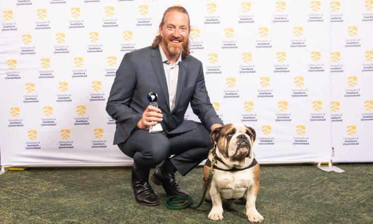 man crouching next to his dog smiling