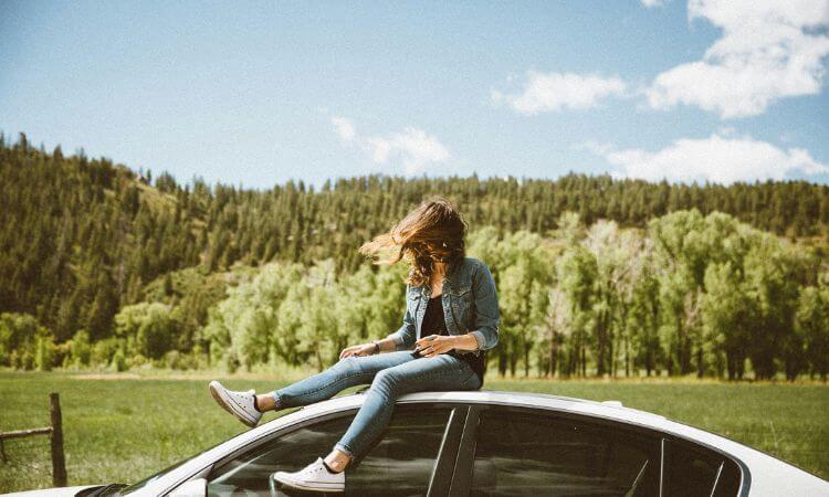 A woman sitting on top of a car in a field.