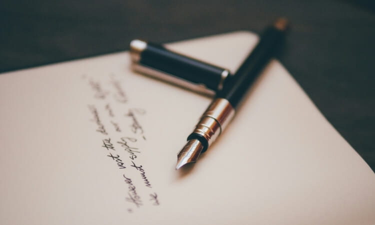 A fountain pen rests on an open notebook with handwritten text.