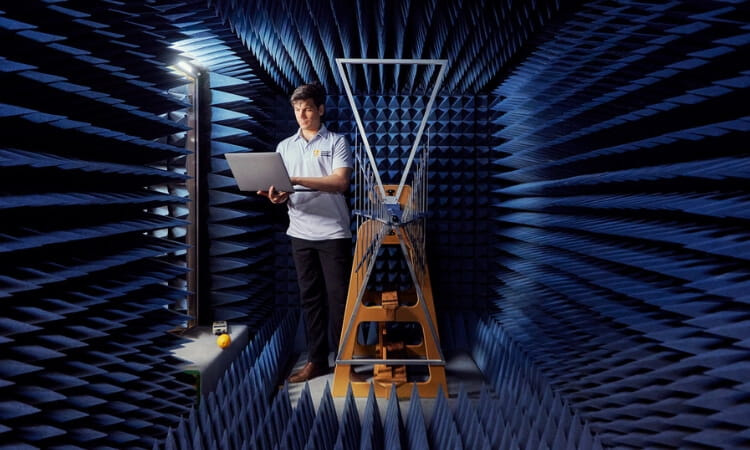 A person stands in an anechoic chamber holding a laptop.