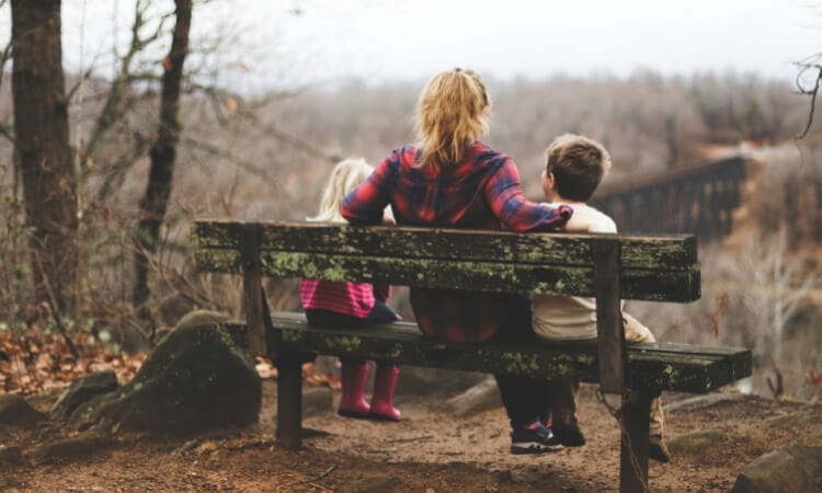 A person sits on a wooden bench with two childre.