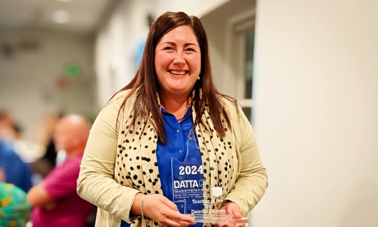 A woman holding a glass award with "2024 DATA Queensland" and "Teacher Award" etched on it.