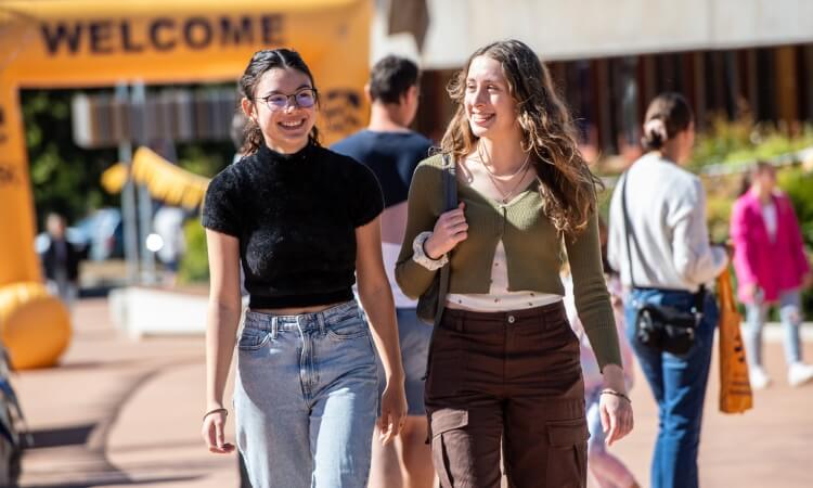 Two women walk and chat in an outdoor setting.