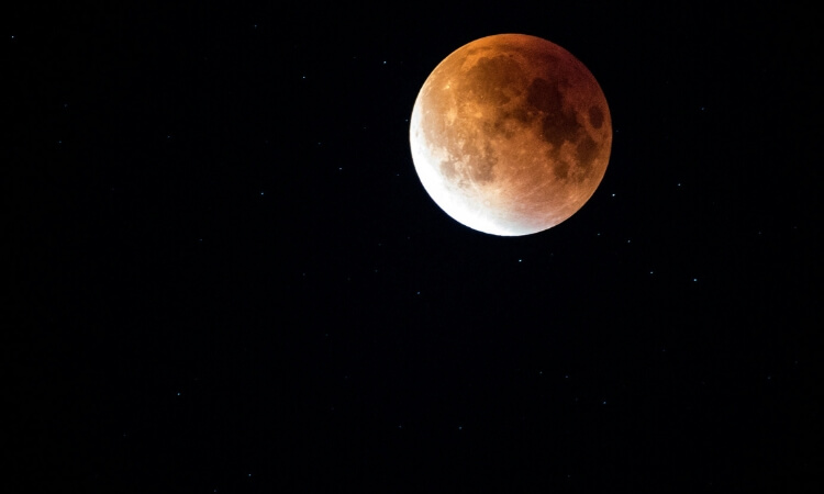 A lunar eclipse with the moon partially covered by Earth's shadow, displaying a reddish hue against a black star-filled sky.