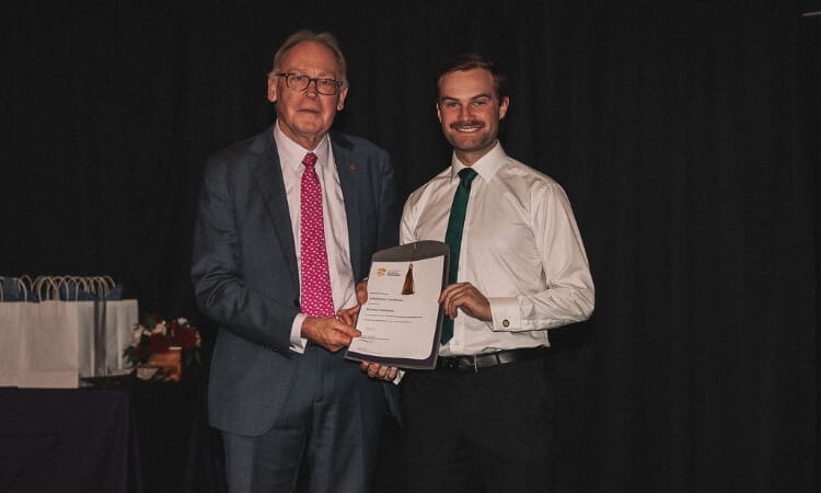 Two men stand on a stage. They are holding a certificate together, smiling at the camera.