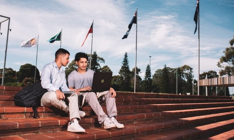 Two people sitting on outdoor steps, looking at a laptop. 