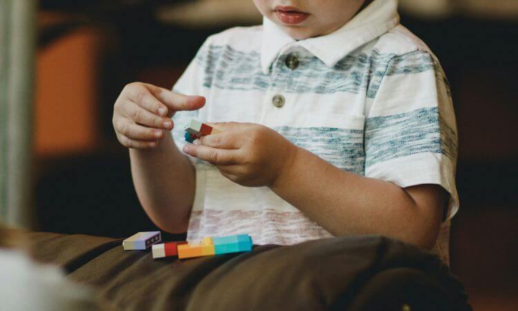 A child in a striped shirt is playing with colorful building blocks, focusing on assembling pieces while seated.