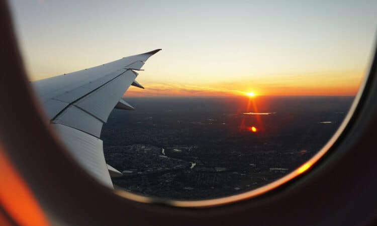 View of an airplane wing from a window with a glowing sunset on the horizon.