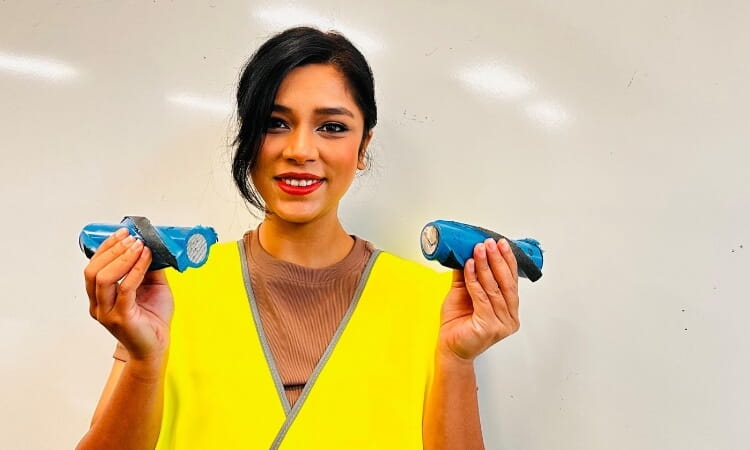 A person wearing a high-visibility vest holds two blue cylindrical devices, smiling in front of a white background.