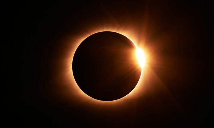 A solar eclipse with the moon covering most of the sun, leaving a bright ring and a small visible portion with a glare on the right side.