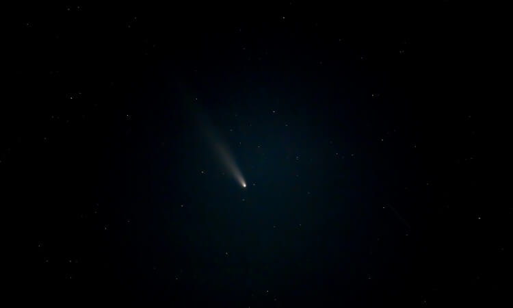 A comet with a glowing tail is visible against a dark, starry night sky.