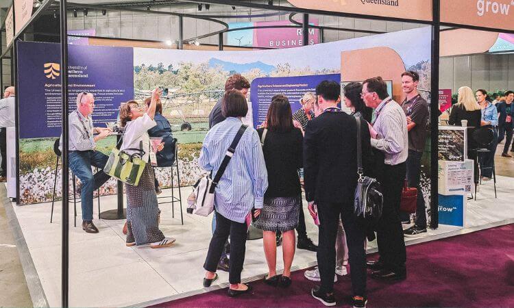 People gather at an agricultural booth during an event, with informational displays and seating areas.