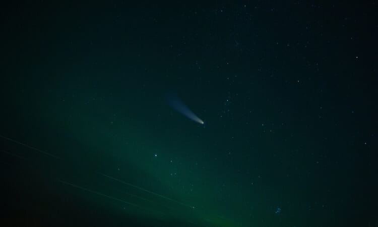 A comet with a visible tail travels across a starry night sky with green aurora bands.