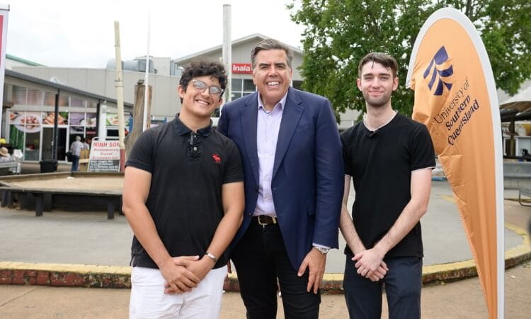 Three men standing in front of a University of Southern Queensland banner outdoors, with buildings and trees in the background.