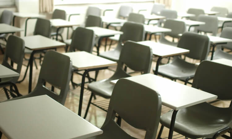 Rows of empty classroom desks and chairs arranged in a neat grid pattern.