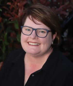 Anita Wheeldon, is smiling in front of a leafy background.